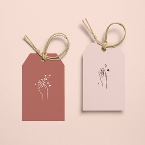 May include: Two gift tags with a hand holding a small branch with stars. The tag on the left is brown and the tag on the right is white.