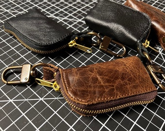 May include: Four leather keychains with zippered pouches and metal clasps. The keychains are brown, black, and a distressed brown color.