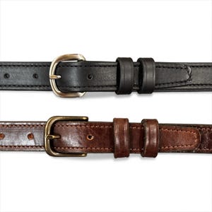 Op de afbeelding: Twee leren riemen met metalen gespen. De bovenste riem is zwart met een zilverkleurige gesp. De onderste riem is bruin met een messingkleurige gesp. Beide riemen hebben een klassiek ontwerp.