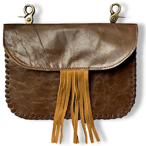 May include: A brown leather crossbody bag with a fringe detail. The bag has a flap closure and two metal clasps.