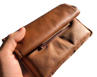 May include: A brown leather wallet with a flap closure. The wallet is folded in half and has a brown leather strap.
