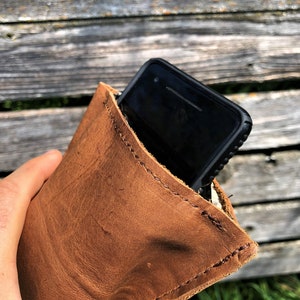 May include: A brown leather phone case with a stitched edge. A black smartphone with a case is inside the leather case.