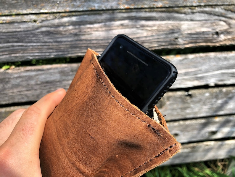 May include: A brown leather phone case with a stitched edge. A black smartphone with a case is inside the leather case.
