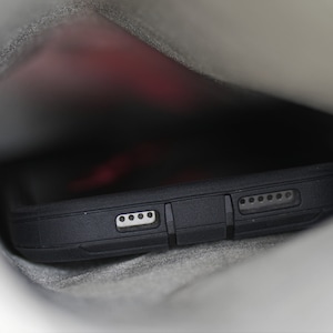 May include: A black phone case with a textured surface and multiple small holes. The case is partially visible inside a gray fabric pocket.