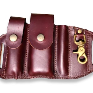 May include: A brown leather belt holster with three pouches and a brass hook. The holster has a stitched design and is made of high-quality leather.