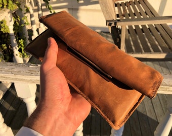 May include: A brown leather clutch purse with a gold metal clasp.