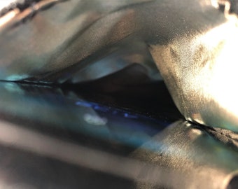 May include: Close-up view of the inside of a black fabric pouch. The pouch is lined with a soft, gold-colored fabric. The inside of the pouch is empty.
