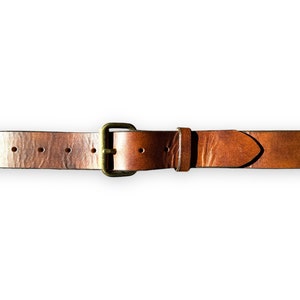 May include: A brown leather belt with a brass buckle. The belt is a medium brown color and has a textured surface. The buckle is rectangular and has a brass finish. The belt is approximately 1.5 inches wide.