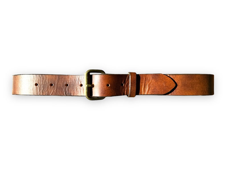 May include: A brown leather belt with a brass buckle. The belt is a medium brown color and has a textured surface. The buckle is rectangular and has a brass finish. The belt is approximately 1.5 inches wide.