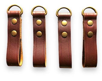 May include: Four brown leather straps with brass rings and two brass rivets each. The straps are approximately 2 inches long.
