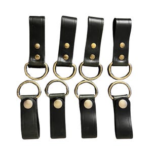 Peut inclure: Six porte-clés en cuir noir avec des anneaux en métal doré et deux points en métal doré. Chaque porte-clés a une boucle en cuir noir.