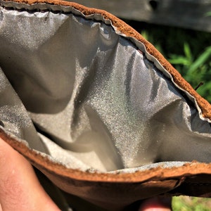 May include: A brown leather pouch with a silver lining. The pouch is open and the lining is visible.