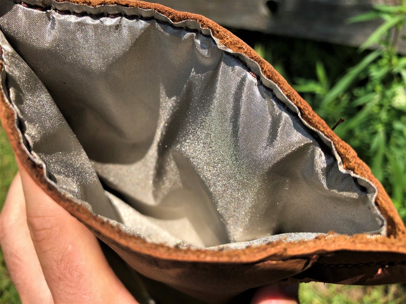 May include: A brown leather pouch with a silver lining. The pouch is open and the lining is visible.
