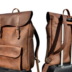 Puede incluir: Una mochila de cuero marrón con cierre de solapa y dos hebillas. La mochila tiene un bolsillo frontal y correas ajustables. La mochila se muestra con las correas extendidas para ser utilizada como asa de maleta.