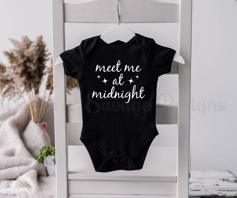May include: Black baby onesie with white text that reads "meet me at midnight" with small stars on either side of the word "at".