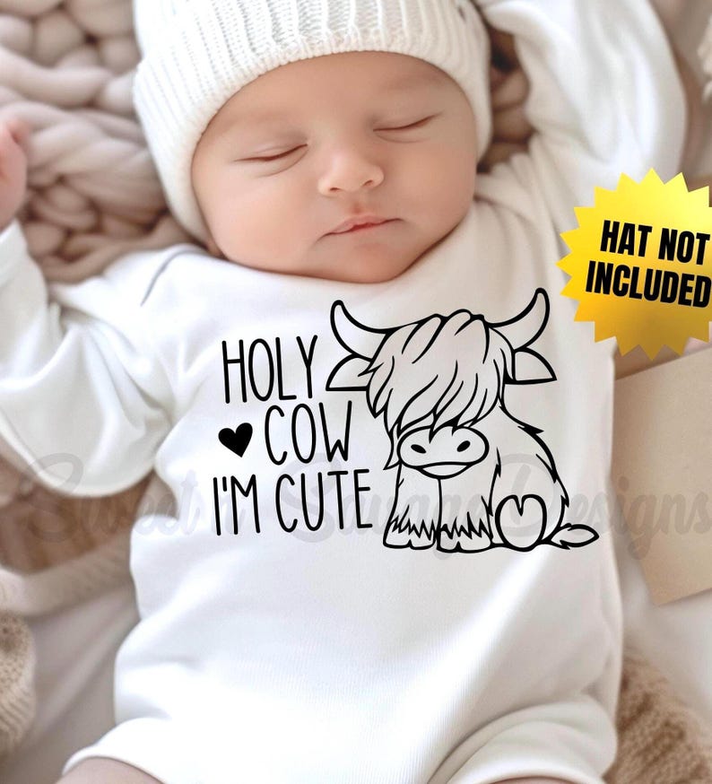 May include: A white long-sleeved baby bodysuit featuring a black graphic of a Highland cow and the text "HOLY COW I'M CUTE" with a heart symbol. A yellow star-shaped graphic on the right side contains the black text "HAT NOT INCLUDED".