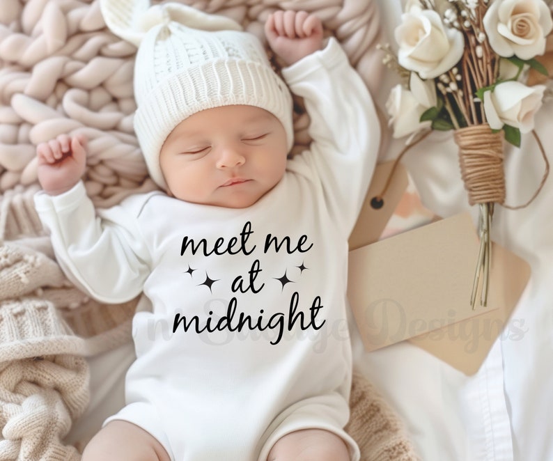 May include: A white baby onesie with black text that reads "meet me at midnight" with two small stars on either side of the word "at". The baby is wearing a white knitted hat and is sleeping on a cream-colored blanket.