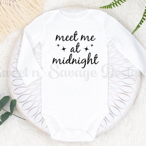 May include: White long-sleeved baby onesie with black text that reads "meet me at midnight" with two small stars on either side of the word "at".