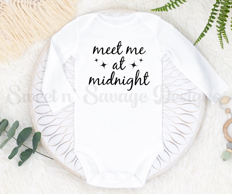 May include: White long-sleeved baby onesie with black text that reads "meet me at midnight" with two small stars on either side of the word "at".