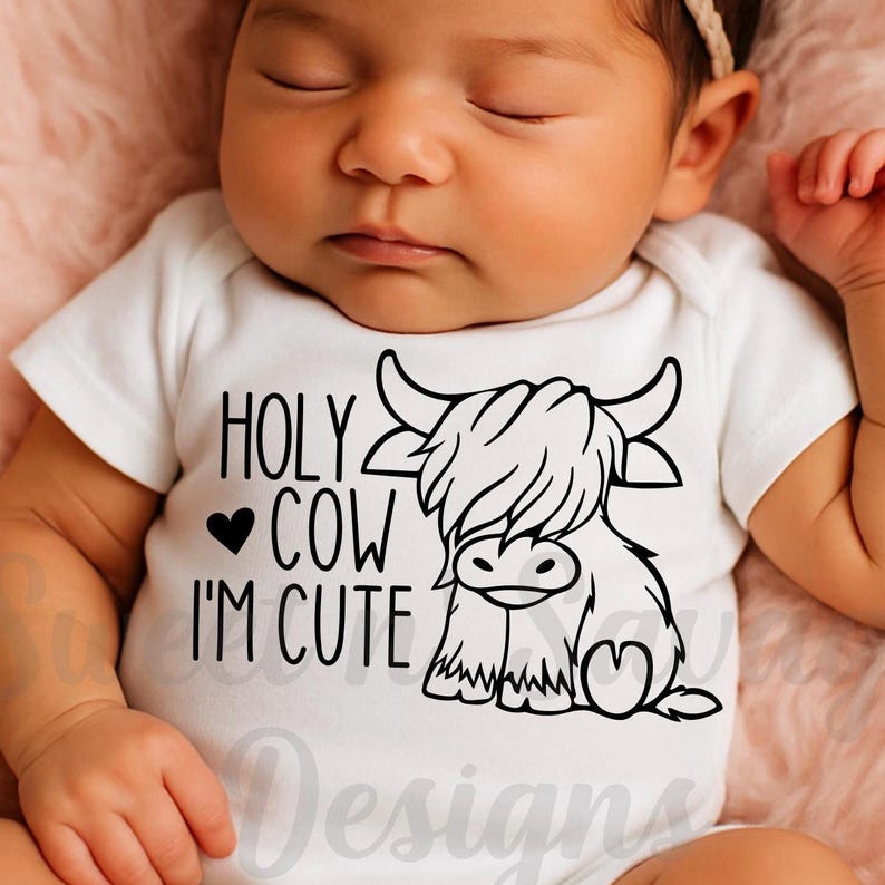 May include: A white short-sleeved baby bodysuit featuring a black graphic print of a Highland cow and the text "HOLY COW I'M CUTE" with a small heart icon. The design is centered on the chest of the garment, which is worn by a sleeping infant.