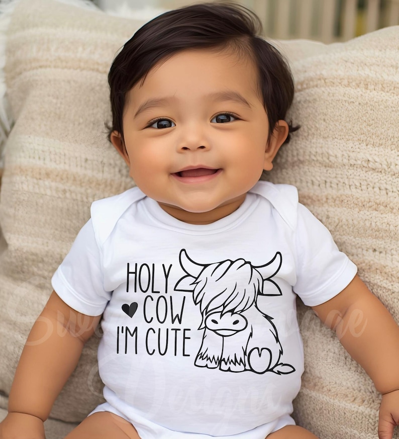 May include: A white short-sleeved baby bodysuit featuring a black graphic print of a Highland cow. The text reads HOLY COW I'M CUTE with a small heart icon. The design is centered on the chest of the garment, which has a simple round neckline.