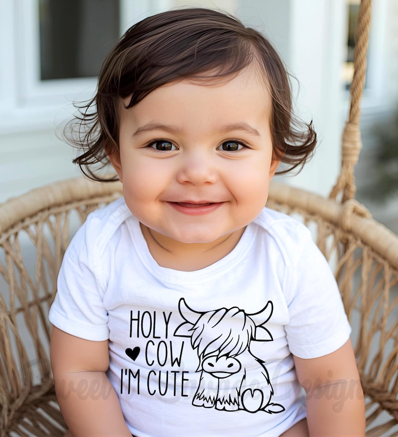 May include: A white short-sleeved baby bodysuit featuring a black graphic print of a Highland cow. The text reads HOLY COW I'M CUTE with a small heart symbol. The design is centered on the chest of the garment, which has a simple round neckline.