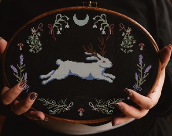 May include: A black embroidery hoop with a white rabbit running with antlers, a crescent moon, and floral designs on a black background.