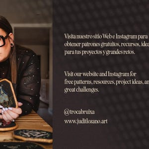 May include: A woman wearing glasses holds a framed embroidery piece with a moon, stars, and a house. The embroidery is surrounded by other framed embroidery pieces on a wooden table. The text on the image reads "Visita nuestro sitio Web e Instagram para obtener patrones gratuitos, recursos, ideas para tus proyectos y grandes retos. Visit our website and Instagram for free patterns, resources, project ideas, and great challenges. @trocabruixa www.juditlozano.art"