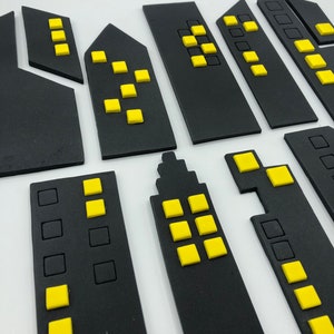 Pode incluir: Um conjunto de formas de edif&iacute;cios de horizonte urbano de espuma preta com janelas amarelas. Os edif&iacute;cios s&atilde;o de v&aacute;rios tamanhos e formas.