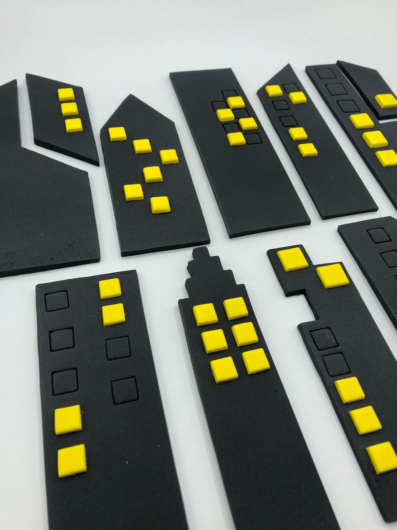 Pode incluir: Um conjunto de formas de edif&iacute;cios de horizonte urbano de espuma preta com janelas amarelas. Os edif&iacute;cios s&atilde;o de v&aacute;rios tamanhos e formas.