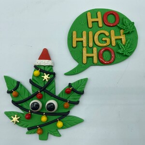 Könnte beinhalten: Ein grüner Weihnachtsbaum in Form eines Marihuana-Blattes mit einer roten Weihnachtsmütze, Kulleraugen und schwarzen Lichterketten mit roten, gelben und orangefarbenen Ornamenten. Eine grüne Sprechblase mit dem Text "HO HIGH HO" in goldenen und roten Buchstaben mit grünen Marihuana-Blättern.