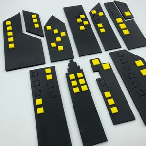 Pode incluir: Um conjunto de dez edif&iacute;cios de cidade de feltro preto com janelas amarelas. Os edif&iacute;cios s&atilde;o de v&aacute;rios tamanhos e formas, e alguns t&ecirc;m mais janelas do que outros.