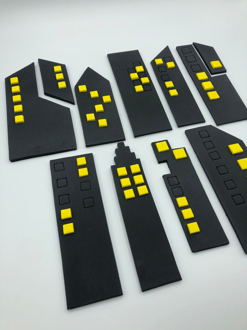 Pode incluir: Um conjunto de dez edif&iacute;cios de cidade de feltro preto com janelas amarelas. Os edif&iacute;cios s&atilde;o de v&aacute;rios tamanhos e formas, e alguns t&ecirc;m mais janelas do que outros.