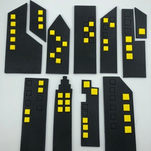 Pode incluir: Um conjunto de 10 toppers de edif&iacute;cios de horizonte da cidade em fondant preto e amarelo. Os edif&iacute;cios s&atilde;o de tamanhos e formas diferentes, alguns t&ecirc;m janelas e outros t&ecirc;m portas.