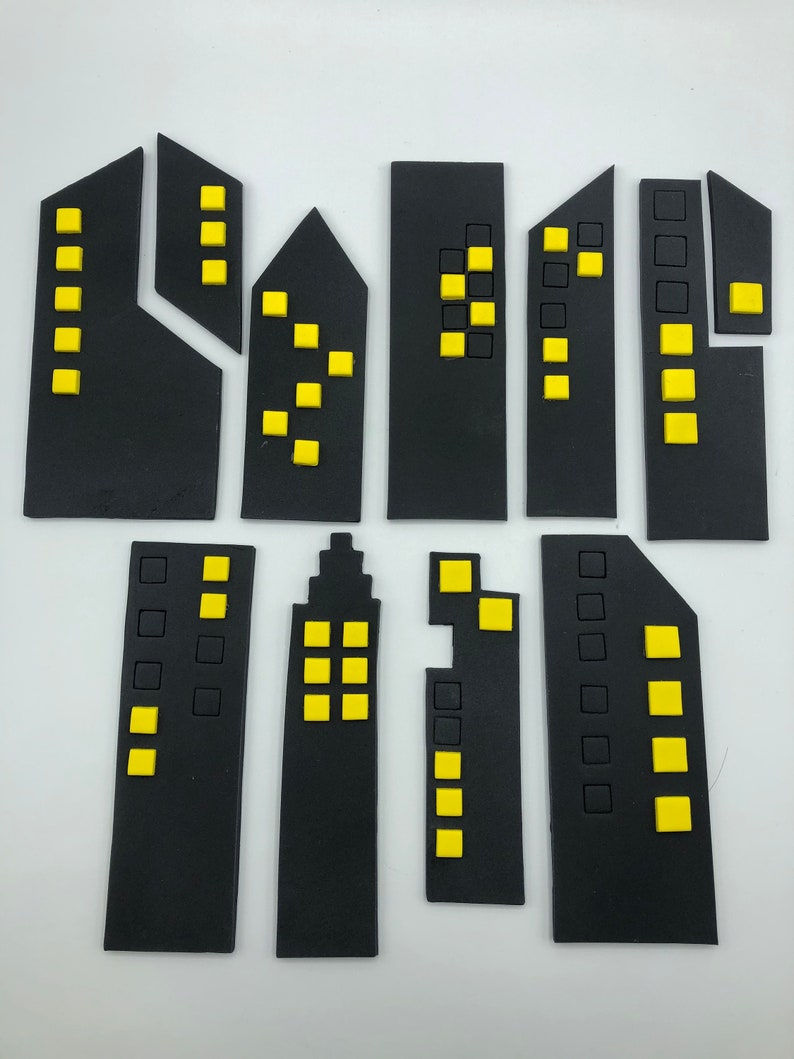 Pode incluir: Um conjunto de 10 toppers de edif&iacute;cios de horizonte da cidade em fondant preto e amarelo. Os edif&iacute;cios s&atilde;o de tamanhos e formas diferentes, alguns t&ecirc;m janelas e outros t&ecirc;m portas.