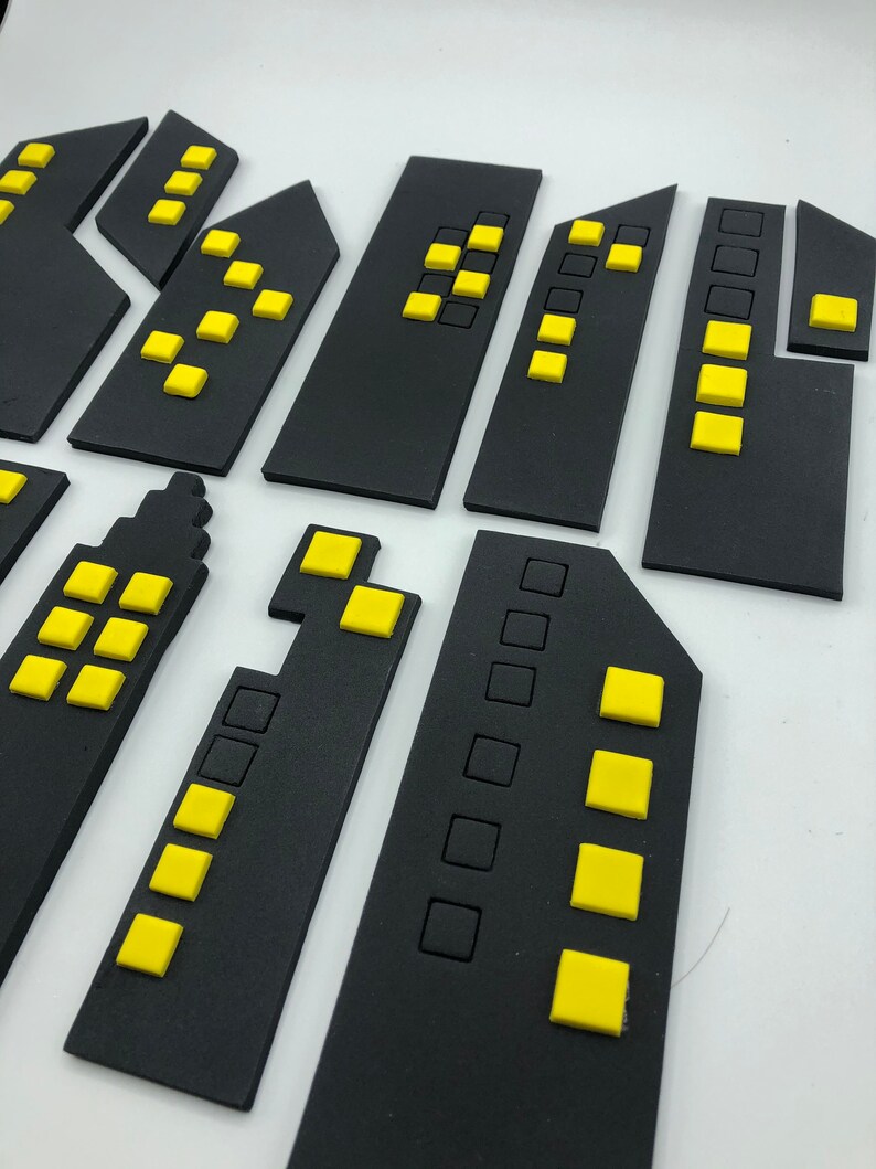 Pode incluir: Silhuetas de cidade de espuma preta com janelas amarelas. As silhuetas est&atilde;o dispostas em fila, com o edif&iacute;cio mais alto no centro.