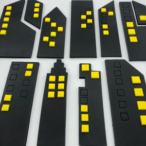 Pode incluir: Um conjunto de 10 formas de edif&iacute;cios de espuma preta em forma de horizonte da cidade com janelas amarelas. Os edif&iacute;cios s&atilde;o de v&aacute;rios tamanhos e formas, e alguns t&ecirc;m telhados arredondados.