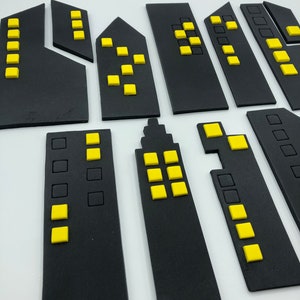 Pode incluir: Um conjunto de blocos de constru&ccedil;&atilde;o de espuma preta com janelas amarelas. Os blocos t&ecirc;m a forma de diferentes edif&iacute;cios, incluindo arranha-c&eacute;us e casas.