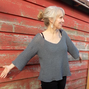 May include: A gray knitted sweater with a v-neck and long sleeves. The sweater is loose fitting and has a relaxed style.