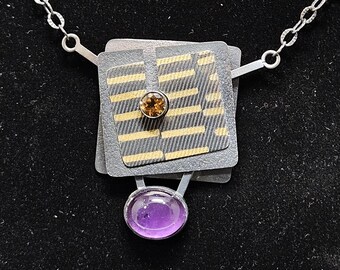 May include: A silver necklace with a geometric pendant featuring a layered square design with gold accents and a small brown gemstone. The pendant is attached to a silver chain and hangs from a purple amethyst gemstone.