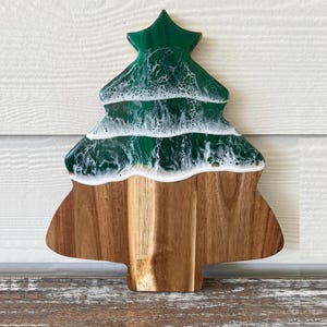 May include: A green and white resin Christmas tree shaped cutting board. The board is made of wood and has a natural wood finish.