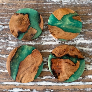 May include: Four round coasters with a unique design. Each coaster features a combination of natural wood and teal-colored resin. The wood has a warm, brown tone with intricate grain patterns, while the resin adds a vibrant pop of color. These coasters are a decorative and functional addition to any home.