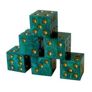 May include: A stack of five six-sided dice with a shimmering emerald green finish and gold-colored pips. The dice are arranged in a pyramid formation, with one die on top, two in the middle, and two at the base, showcasing the metallic texture.