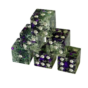 May include: Six clear dice with white pips are stacked in a pyramid shape. The dice have a green and purple glittery interior. The dice are cube-shaped and have rounded corners.