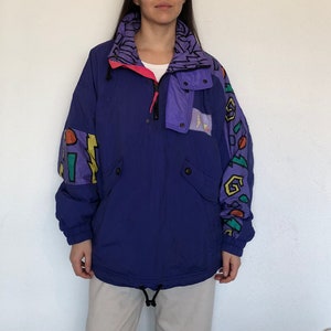 Può includere: Una giacca da sci con motivo viola, blu, verde e giallo con chiusura a zip. La giacca ha un colletto alto e una fodera viola.