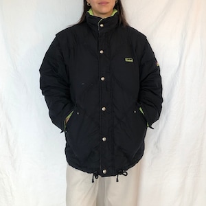 Peut inclure: Veste matelassée noire avec un motif matelassé en losange et une fermeture éclair verte. La veste a un col montant et une fermeture à pression. Le nom de la marque "Salomon" est visible sur le devant de la veste.