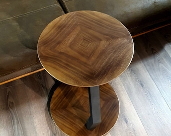 May include: A round wooden side table with a dark brown wood top and a black metal base. The table has a unique design with a diamond pattern in the wood.