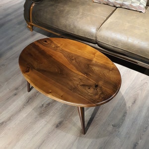 May include: A wooden oval-shaped coffee table with a dark brown wood grain finish and black metal legs.