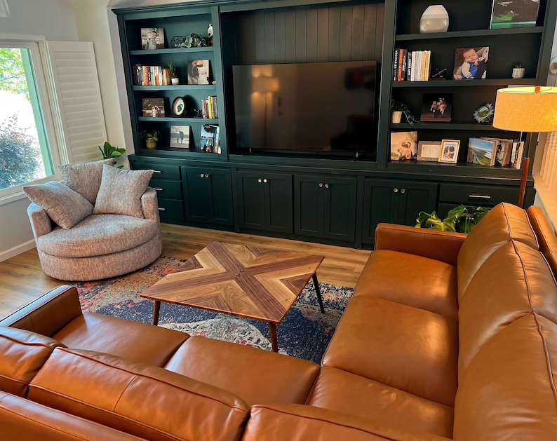 May include: A living room with a dark green built-in entertainment center, a brown leather sectional sofa, a round gray swivel chair, and a wooden coffee table with a geometric pattern.