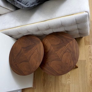 K&ouml;nnte beinhalten: Zwei runde Holz-Beistelltische mit einer dunkelbraunen Holzmaserung. Die Tische stehen auf einem hellbraunen Holzboden.